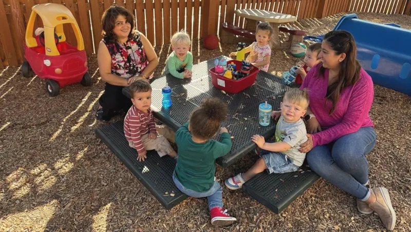 Young children and teachers at a picnic table outside